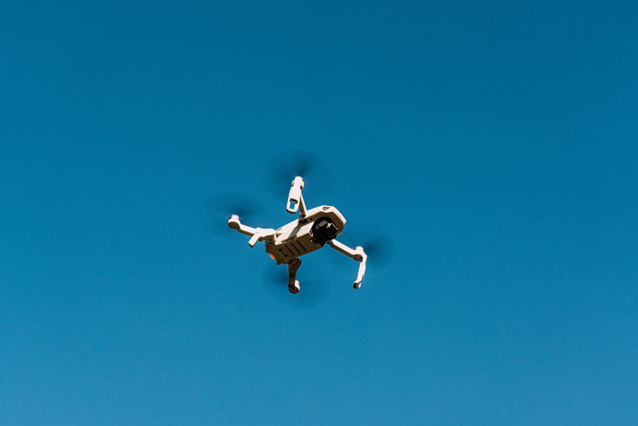 A drone flying against a clear blue sky, capturing aerial views.